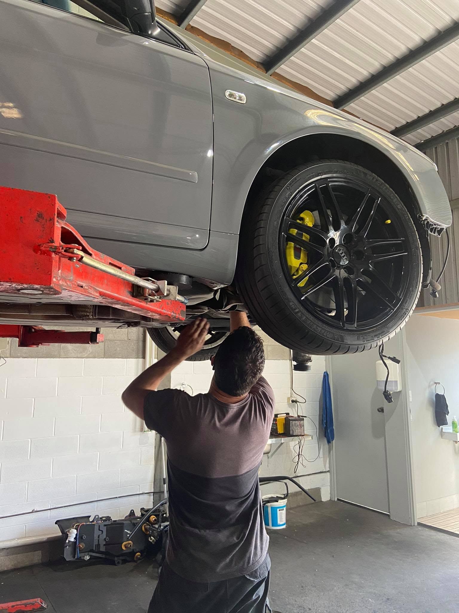 Mechanic Working Under a Gray Car Lifted on a Red Hoist in a Garage — AA Automotive Repairs in Forster, NSW