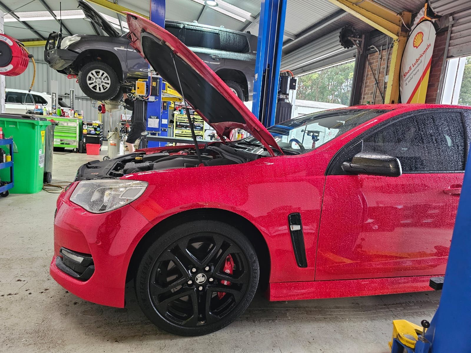 Red Car in an Auto Shop With Its Hood Open and a Wheel Removed on a Lift — AA Automotive Repairs in Forster, NSW