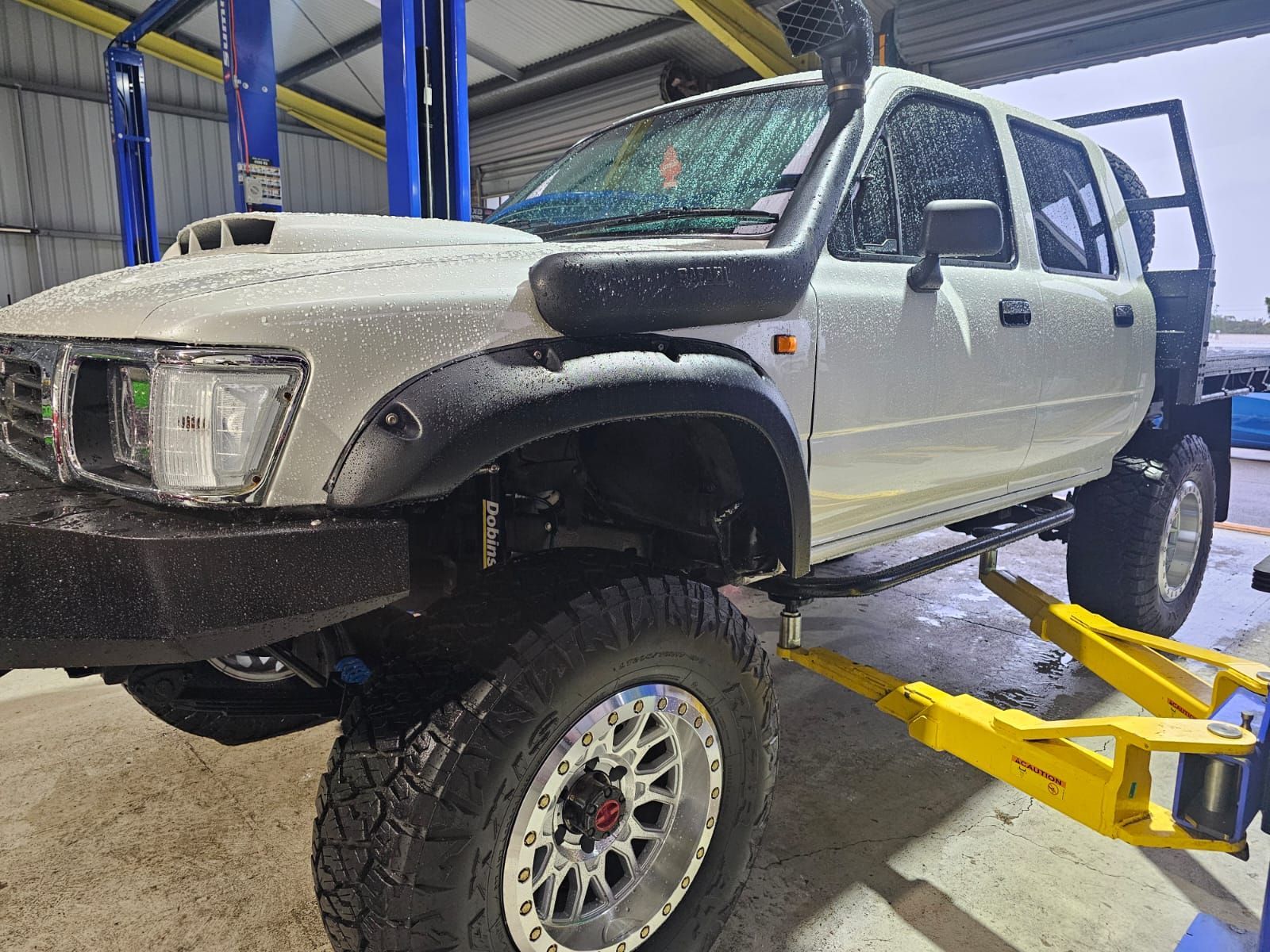 White SUV on a Lift in an Auto Shop, Front End Damaged and a Tire Removed — AA Automotive Repairs in Forster, NSW