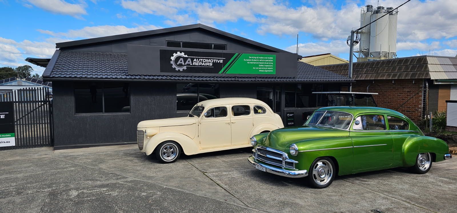 Two Classic Cars, Cream and Green, Parked Outside a Black Garage Under a Blue Sky — AA Automotive Repairs in Forster, NSW