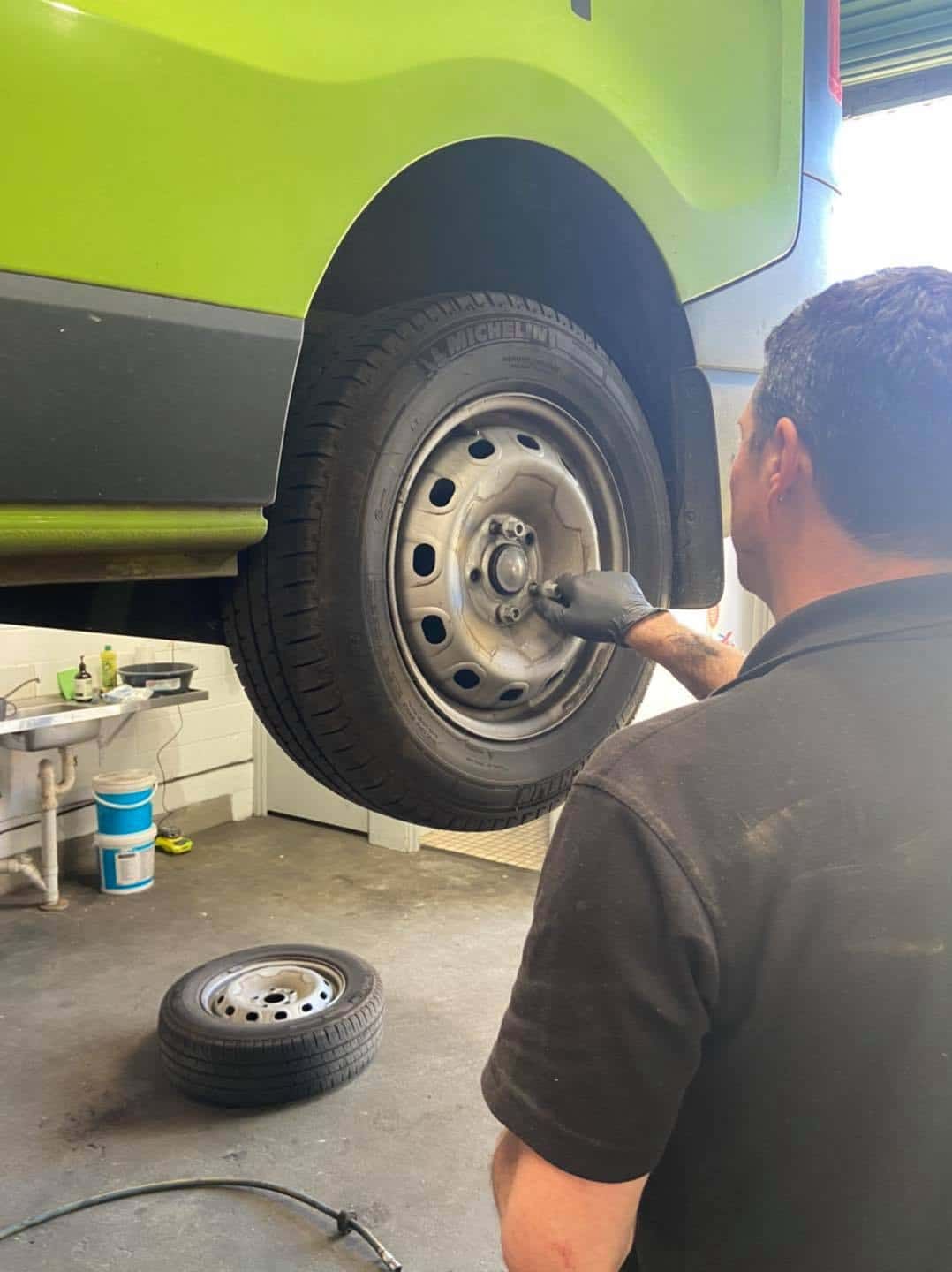 A Man is Changing a Tyre on a Green Van in a Garage — AA Automotive Repairs in Forster, NSW