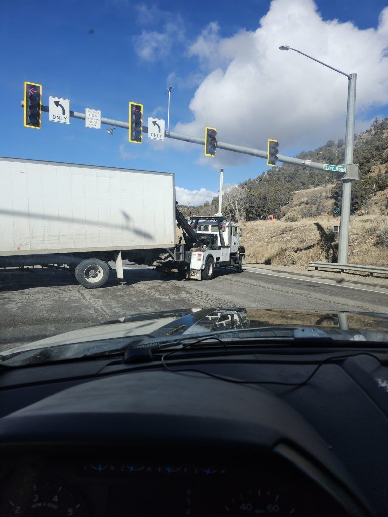Semi truck turning through an intersection under traffic lights on a sunny day, viewed from inside a car.
