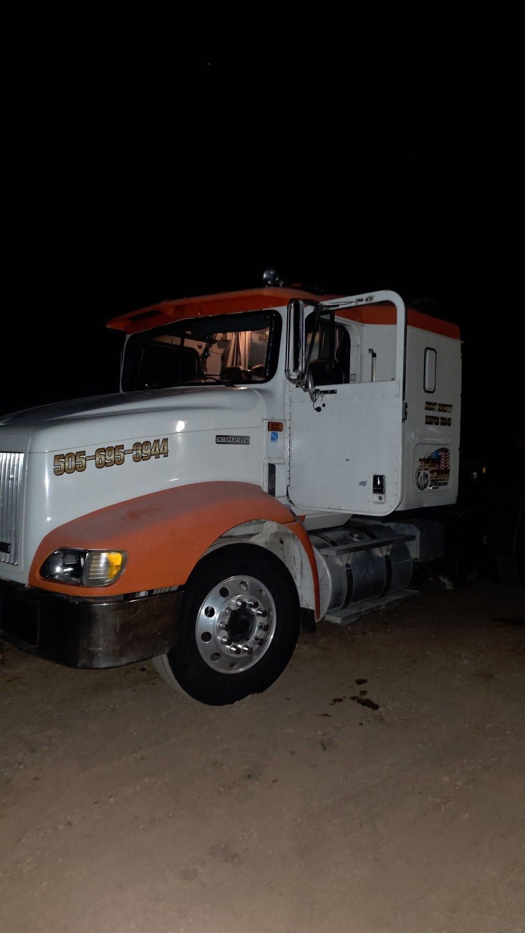 White-and-orange semi truck parked at night on a dirt surface.
