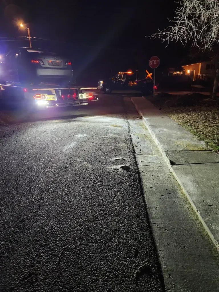 Police car with flashing lights blocking a wet street at night, near a stop sign and sidewalk.
