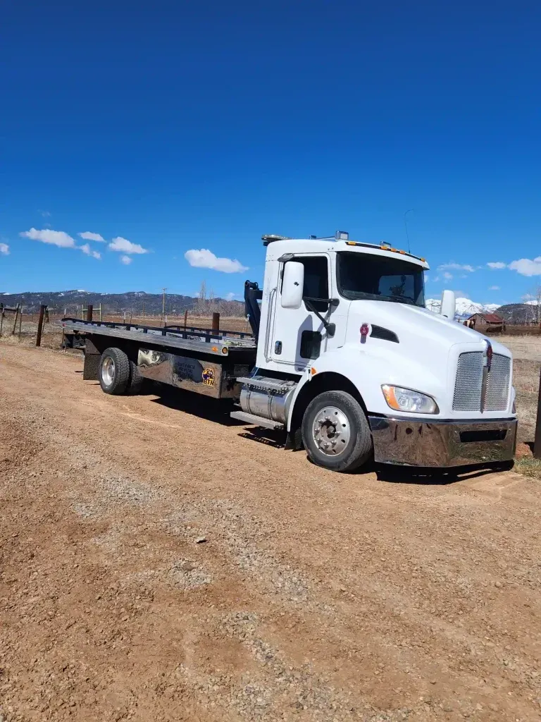 White flatbed tow truck parked on a dirt lot under a clear blue sky