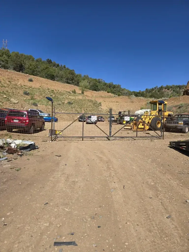 Locked gate at a dirt road construction yard with parked trucks and heavy machinery under a clear blue sky