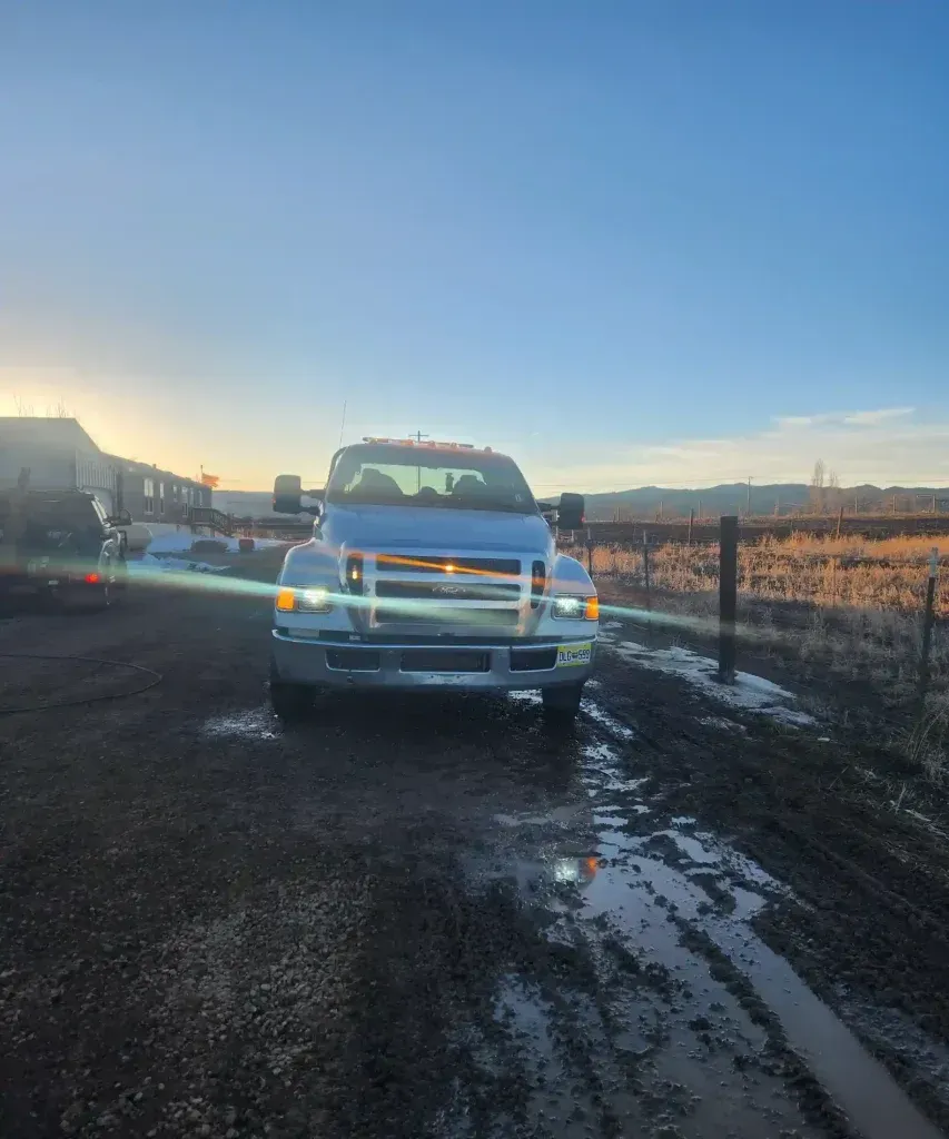 White pickup truck on a muddy rural road at sunset, with fields and a blue sky in the background