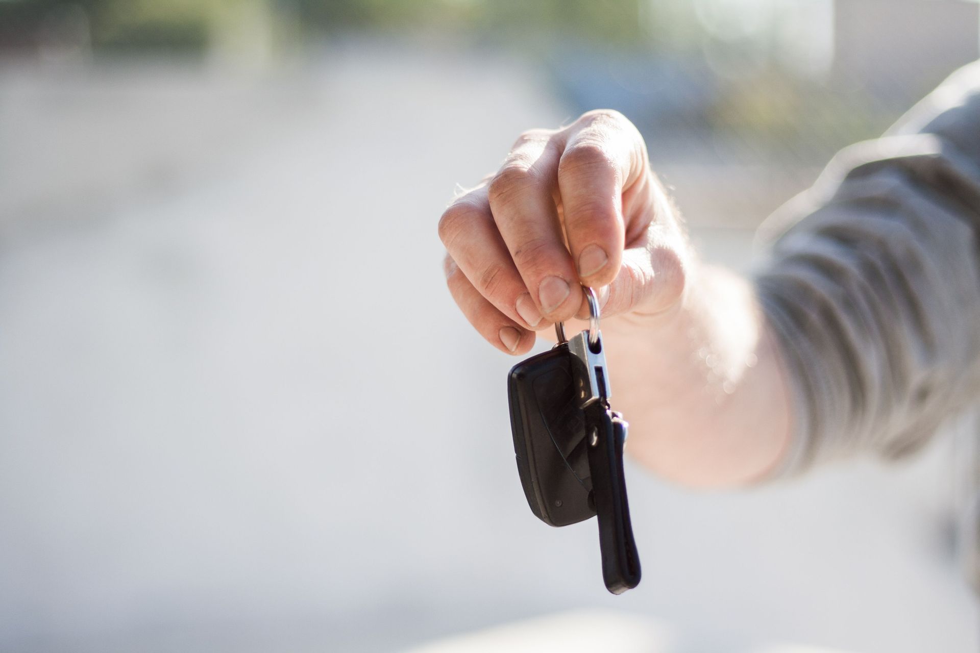 Hand holding car keys with a black key fob against a blurred outdoor background