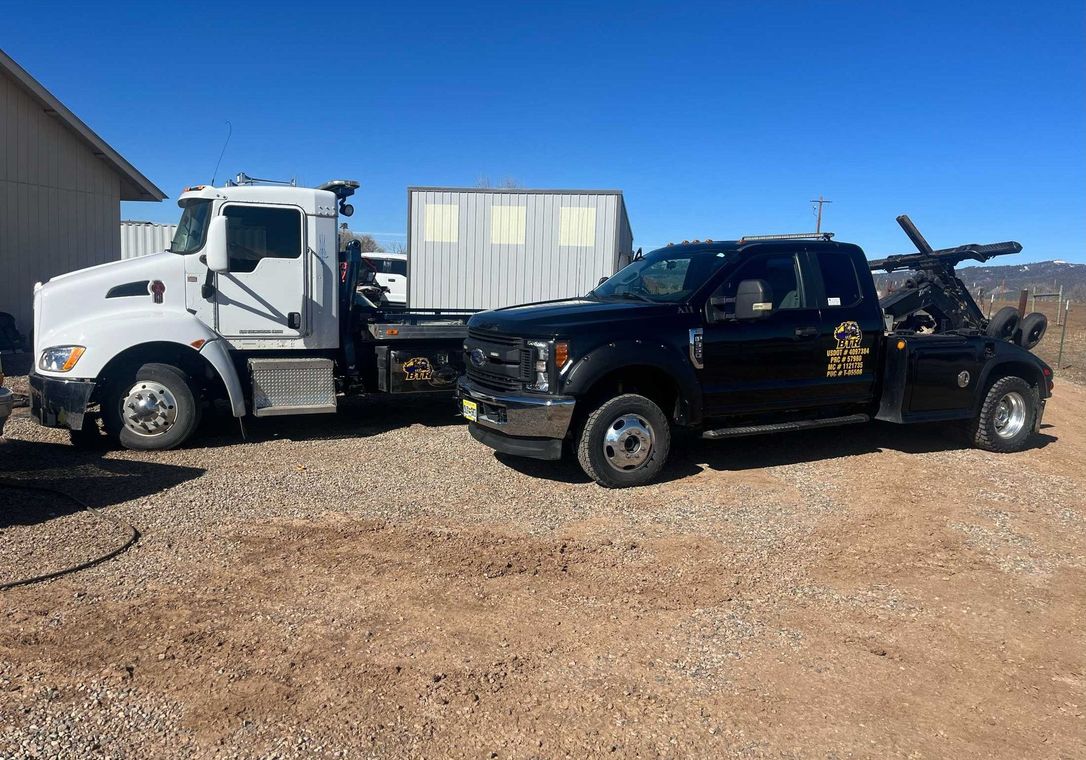 White and black tow trucks parked side by side on a gravel lot under a clear blue sky