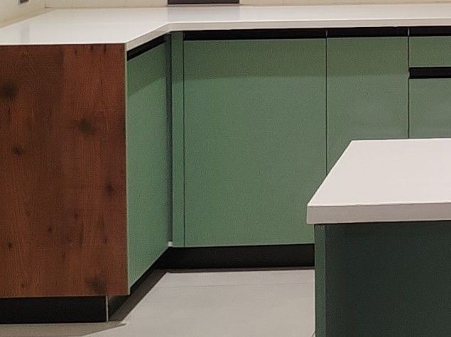 Empty kitchen with green cabinets, white countertops, and a wooden cabinet on the left.