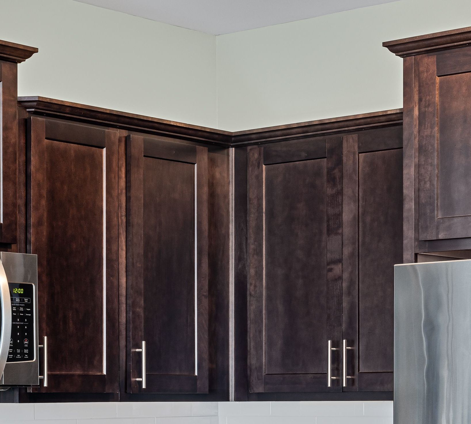 Dark wood kitchen cabinets with silver handles and part of a stainless steel refrigerator.