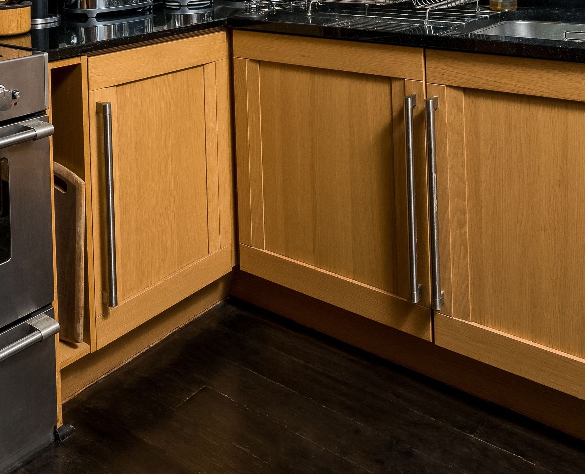 Wooden kitchen cabinets with a slightly open corner door and dark floor tiles underneath