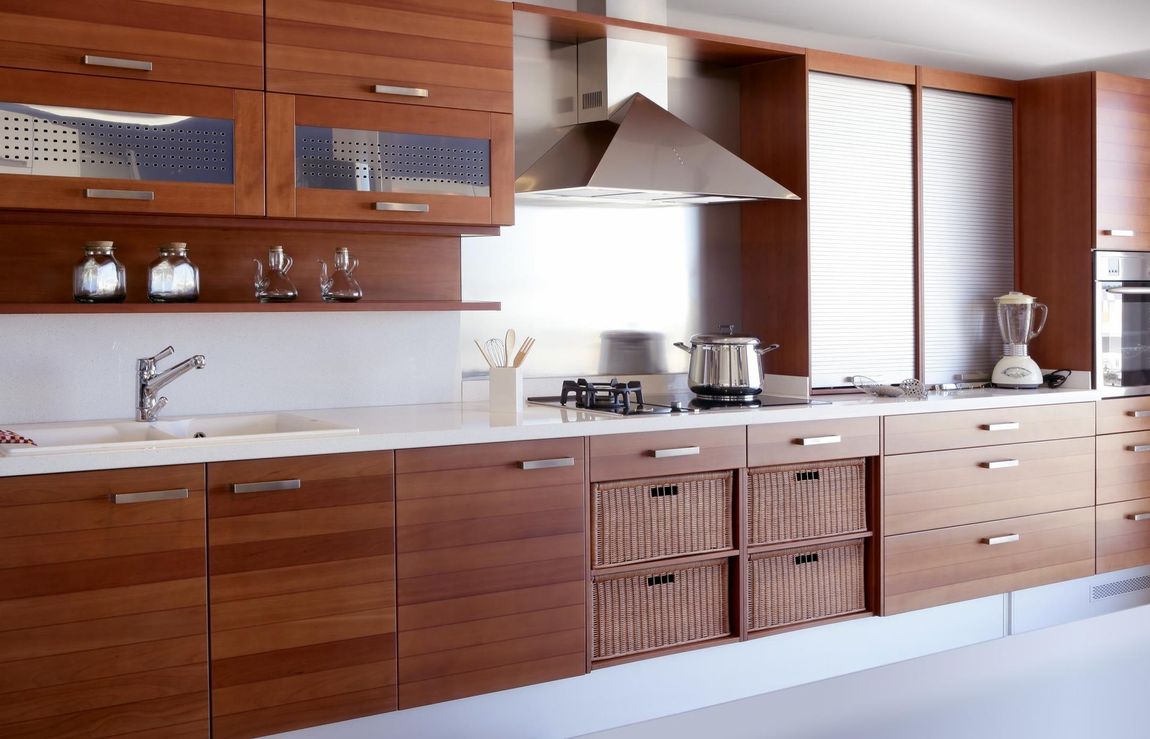 Modern wooden kitchen with white countertops, stainless hood, shelves, and wicker cabinet drawers