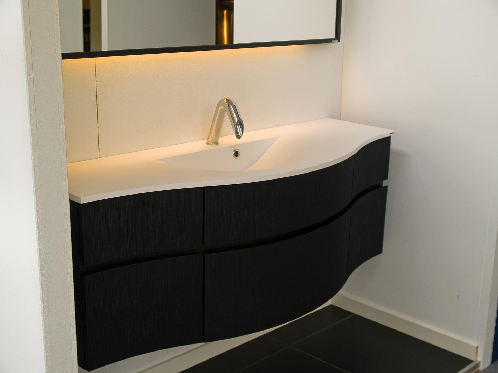 Modern bathroom vanity with white sink, chrome faucet, and black curved cabinet beneath a mirror.