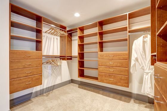 Spacious walk-in closet with wooden shelves, drawers, hanging rods, and beige carpet.