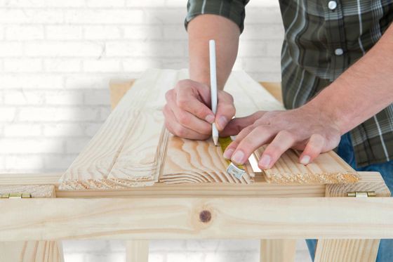 Hands marking measurements on a wooden plank with a pencil and ruler in a workshop