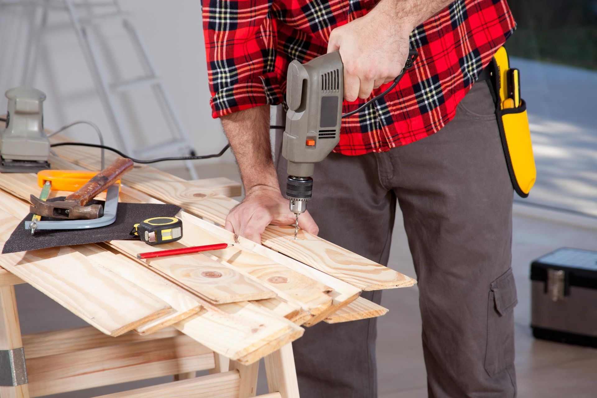 Person using a drill on wooden planks at a workbench in a workshop
