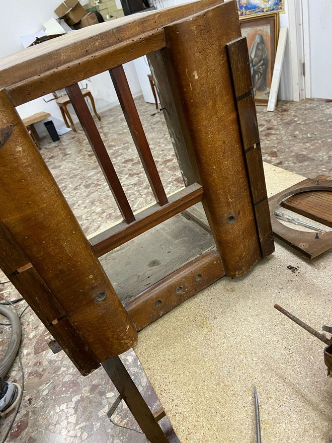 Artigiano del legno al lavoro su una sedia antica durante un restauro accurato.