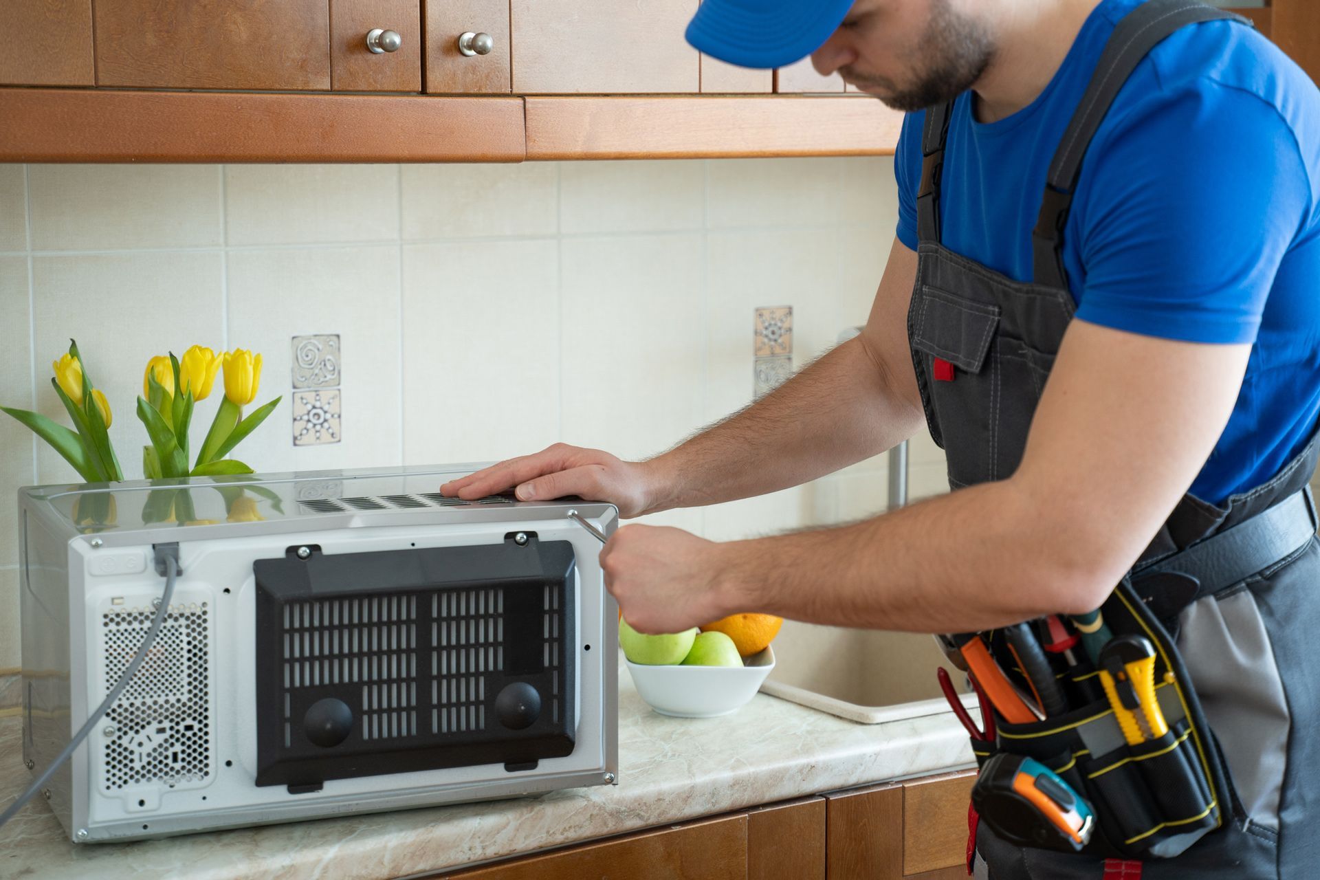 A man is fixing a microwave in a kitchen.