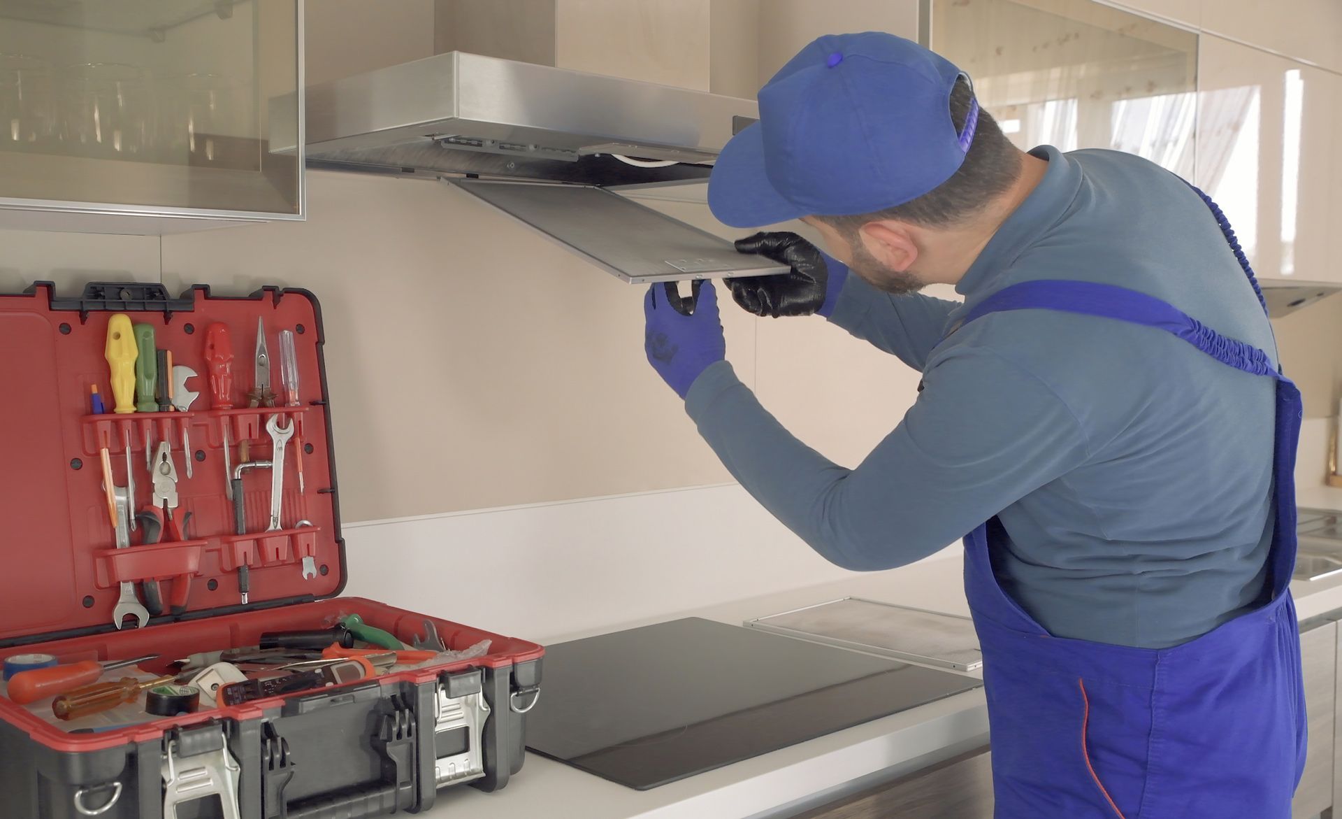 A man is fixing a stove hood in a kitchen.