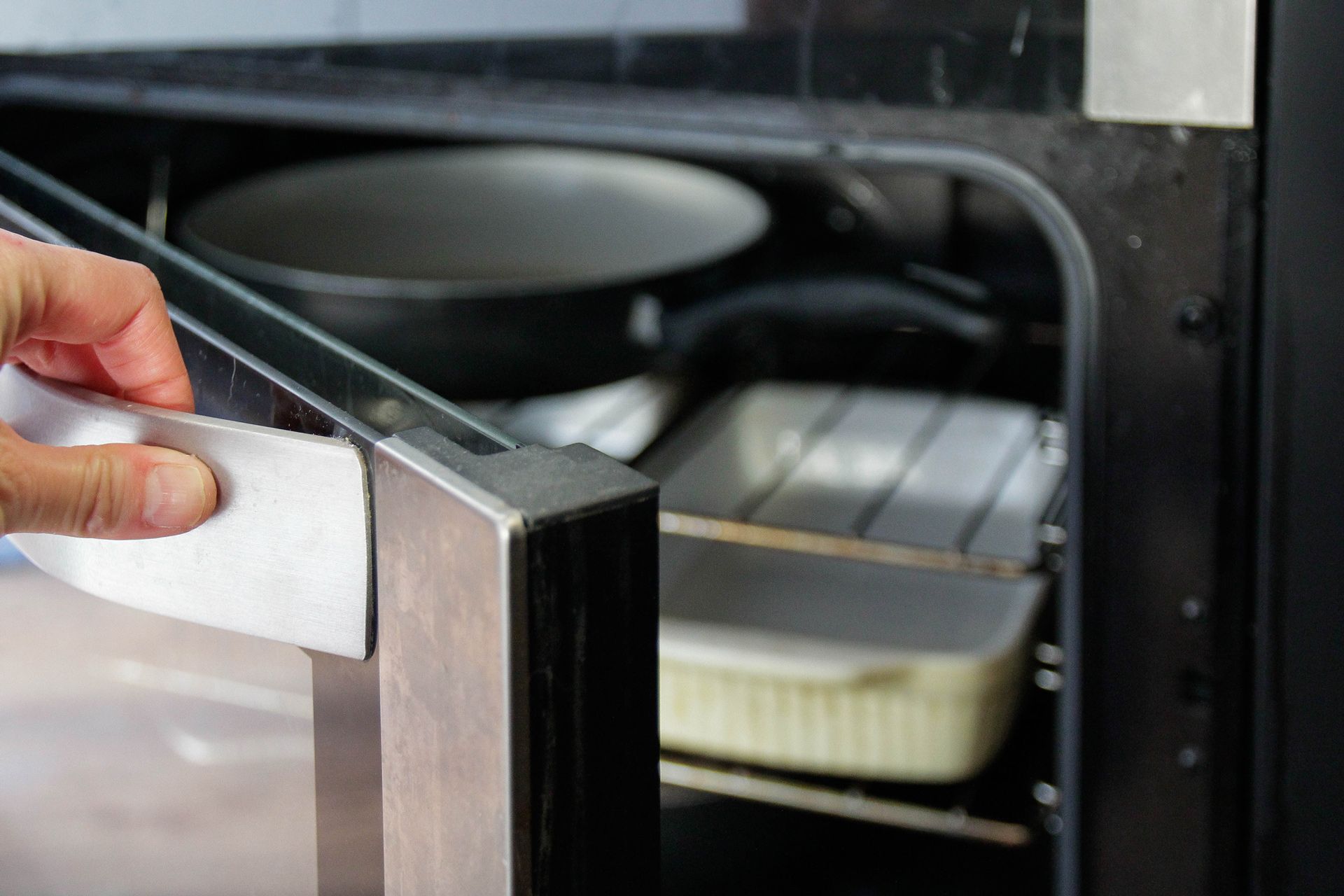 A person is cleaning the door of an oven with a sponge.