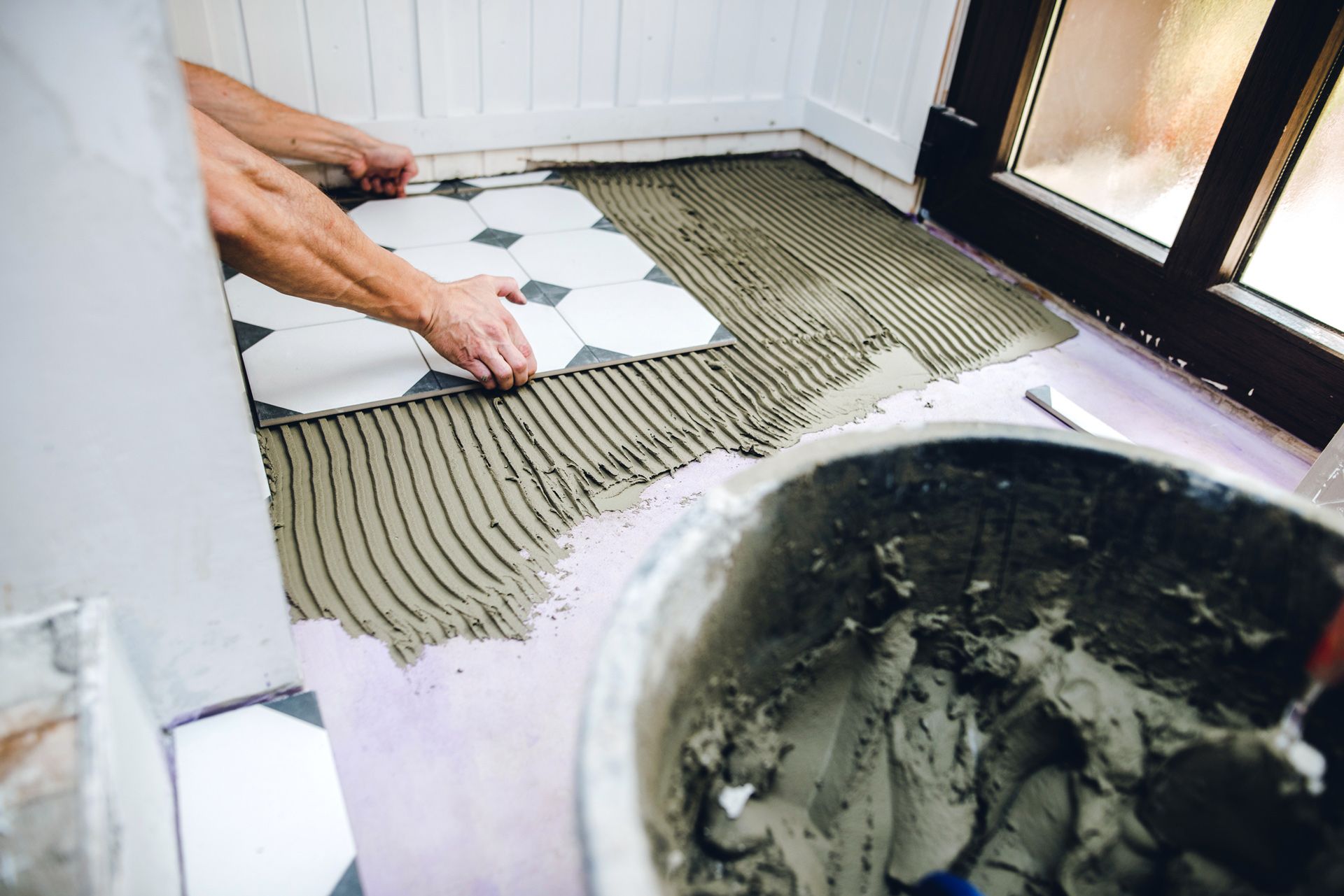 A person is laying tiles on a bathroom floor.