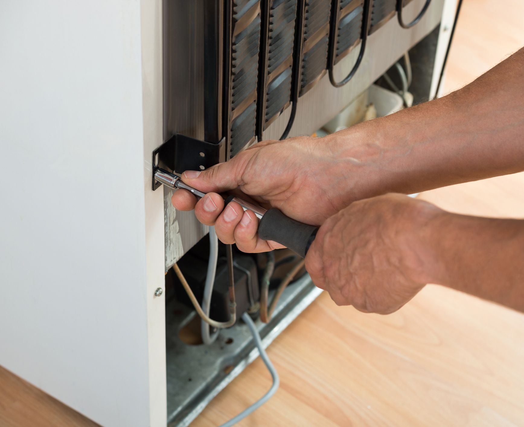 A man is fixing a refrigerator with a screwdriver.