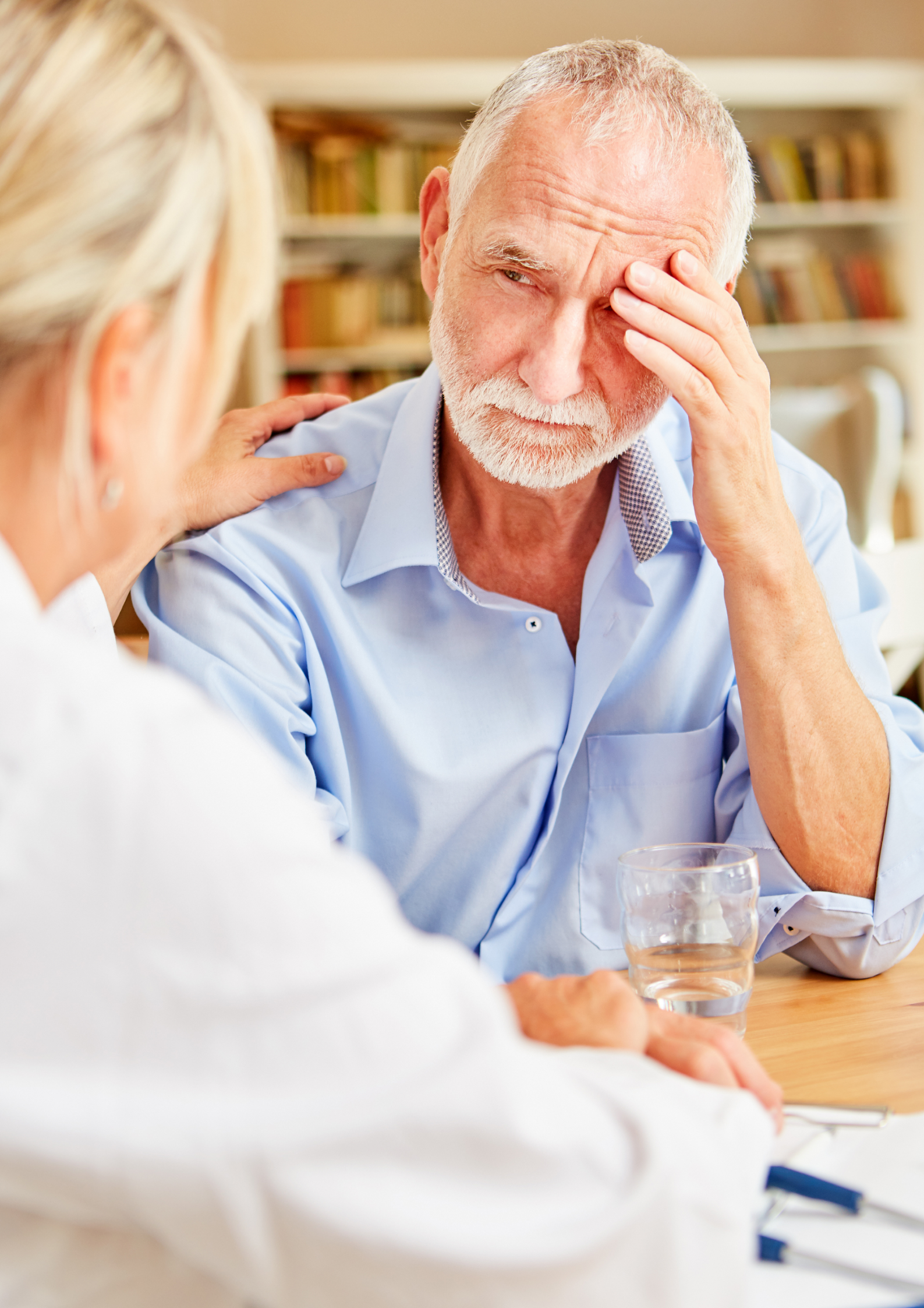 Doctor comforting elderly man, hand on shoulder. He looks distressed, indoors.
