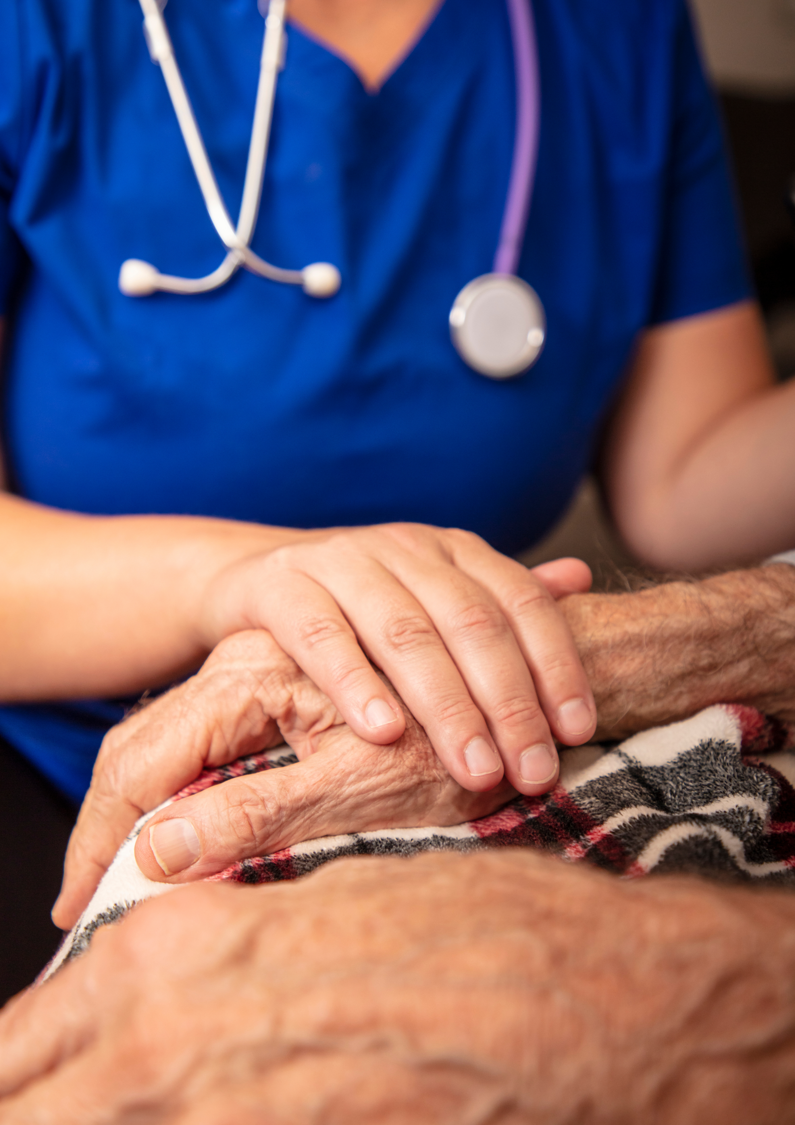 Nurse in blue scrubs holds hands with patient, offering comfort.