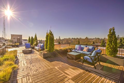Rooftop patio with blue couches, greenery, and sunny sky overlooking a city.