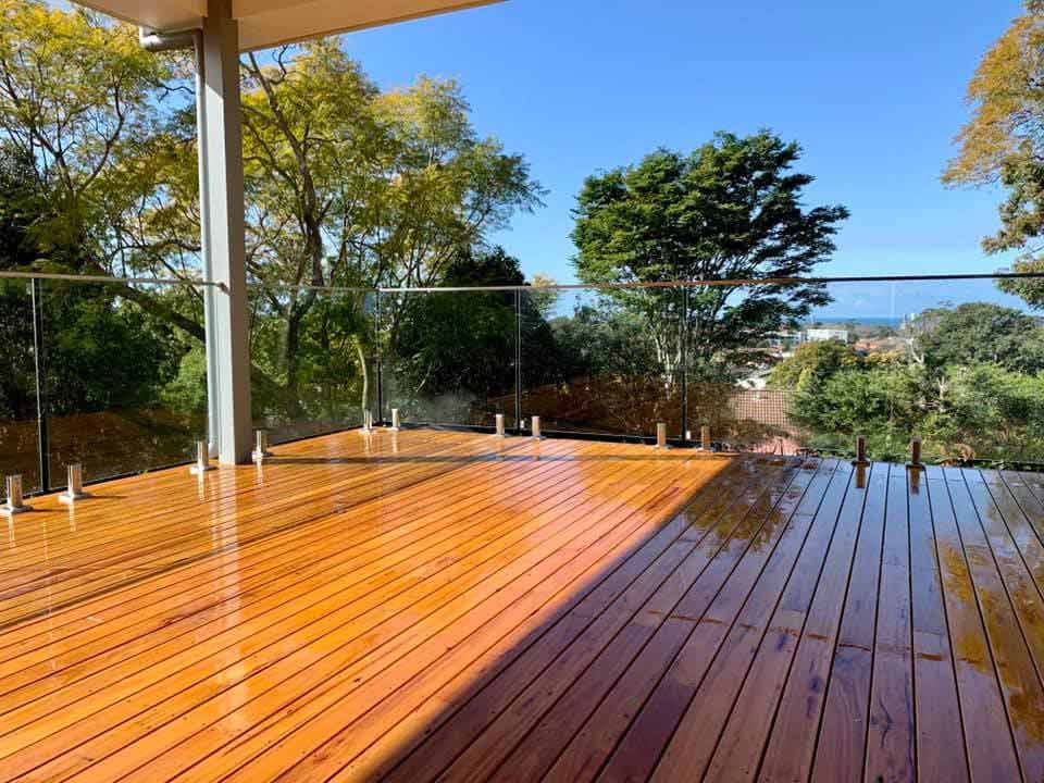 A Wooden Deck With a Glass Railing and Trees in the Background — Craig Allman Construction Pty Ltd In Fernhill, NSW