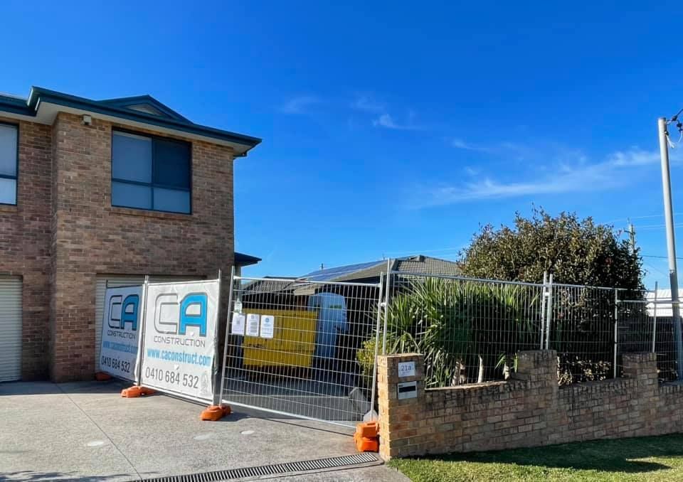 A Brick House is Behind a Fence With a Sign That Says CA Construction — Craig Allman Construction Pty Ltd In Fernhill, NSW
