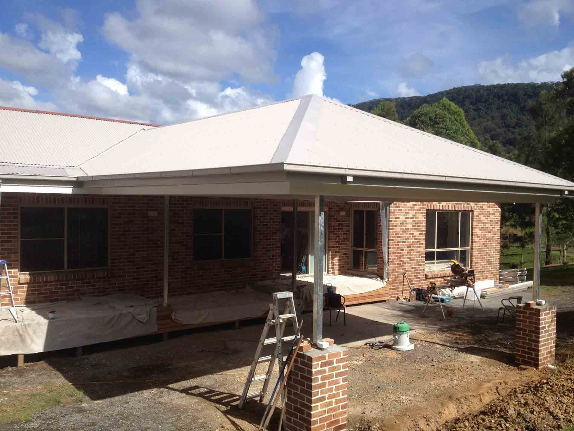A brick house with a white roof and a ladder in front of it — Craig Allman Construction Pty Ltd In Thirroul, NSW