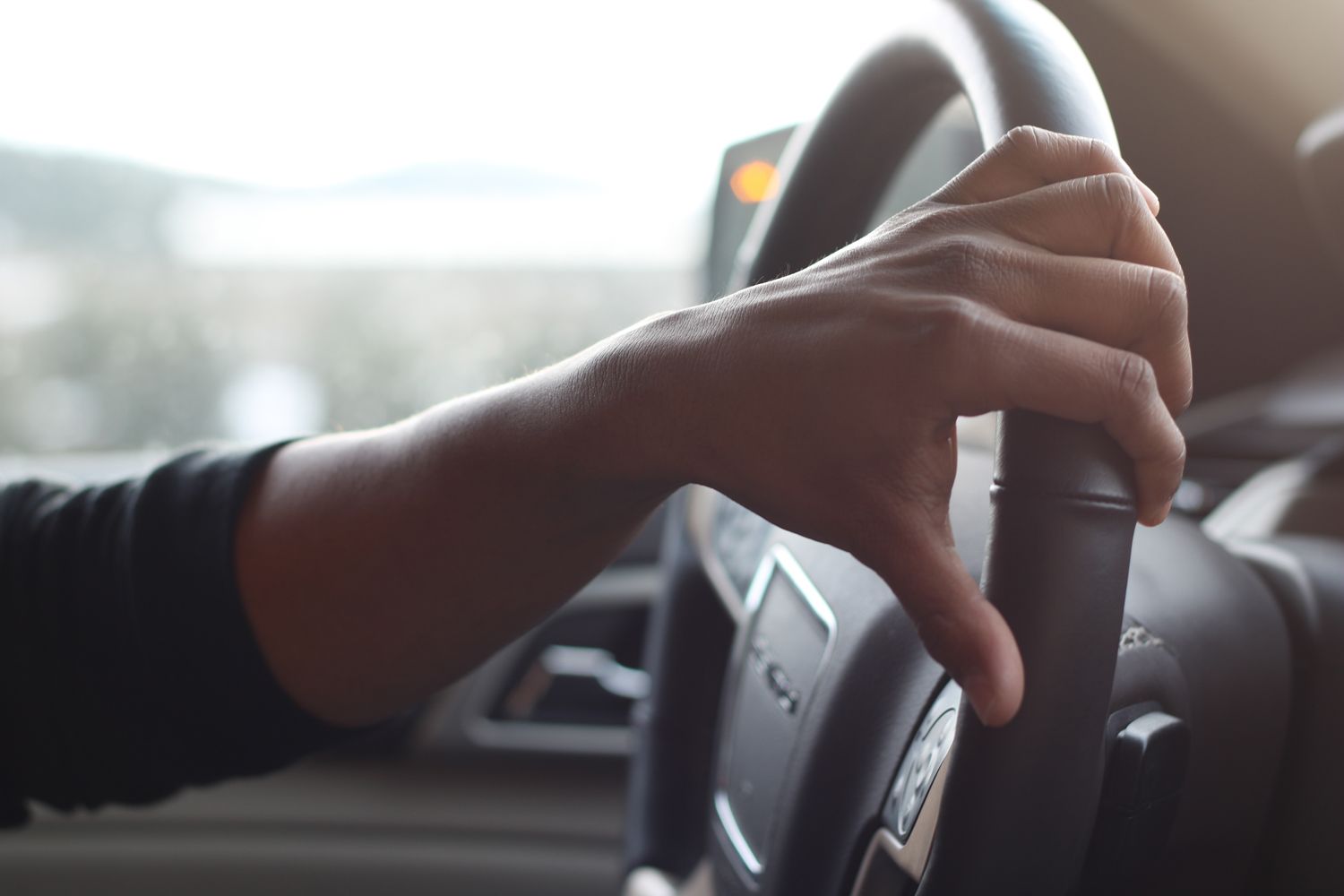 A person's hand gripping a car's steering wheel.