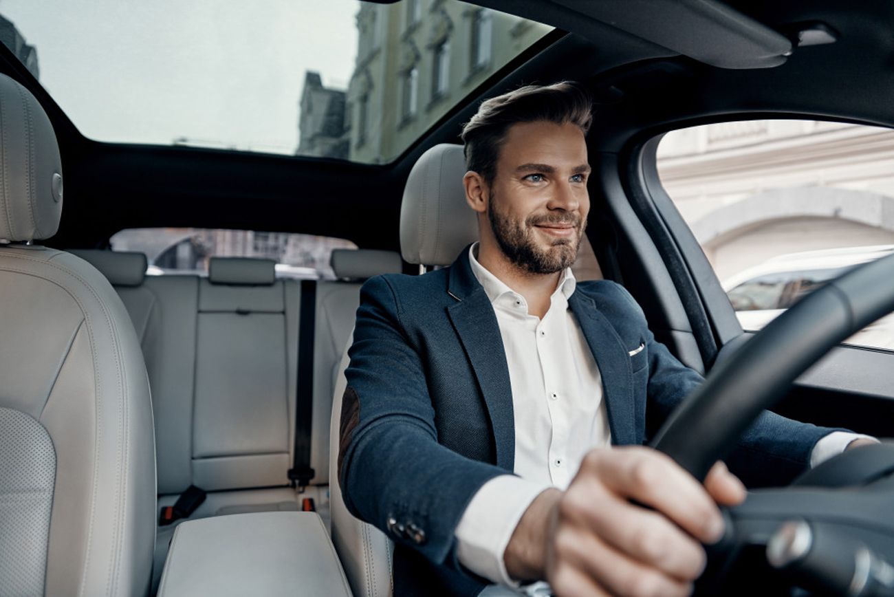 Man in a suit driving a car and smiling.