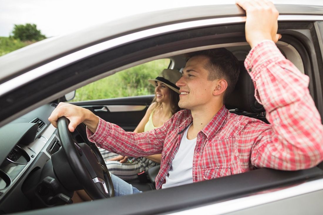 Couple enjoying a road trip, with the man driving and the woman in the passenger seat smiling.