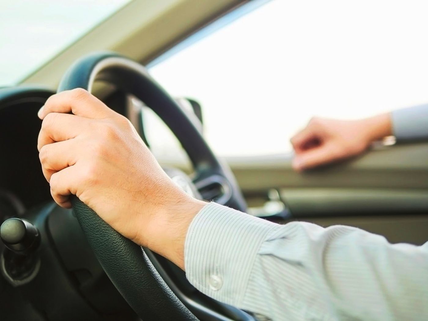 Person holding a car steering wheel with one hand.