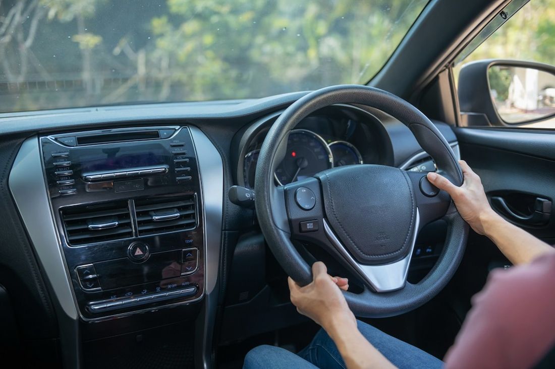 Driver holding the steering wheel of a mercedes-benz car from the driver's seat perspective.