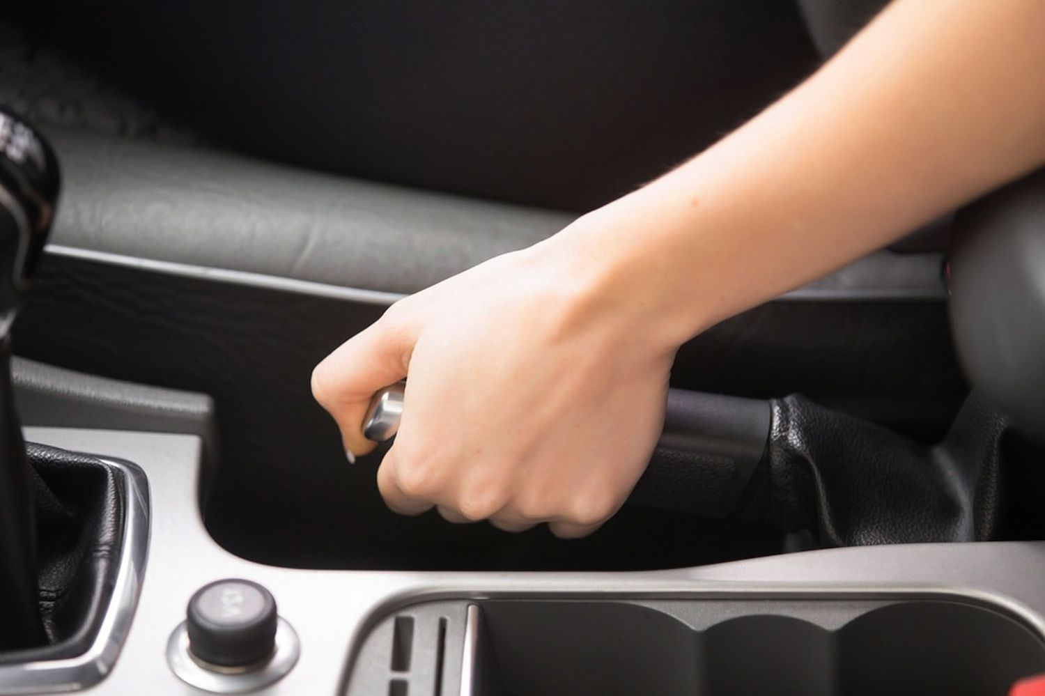 A person's hand engaging the parking brake lever in a vehicle.