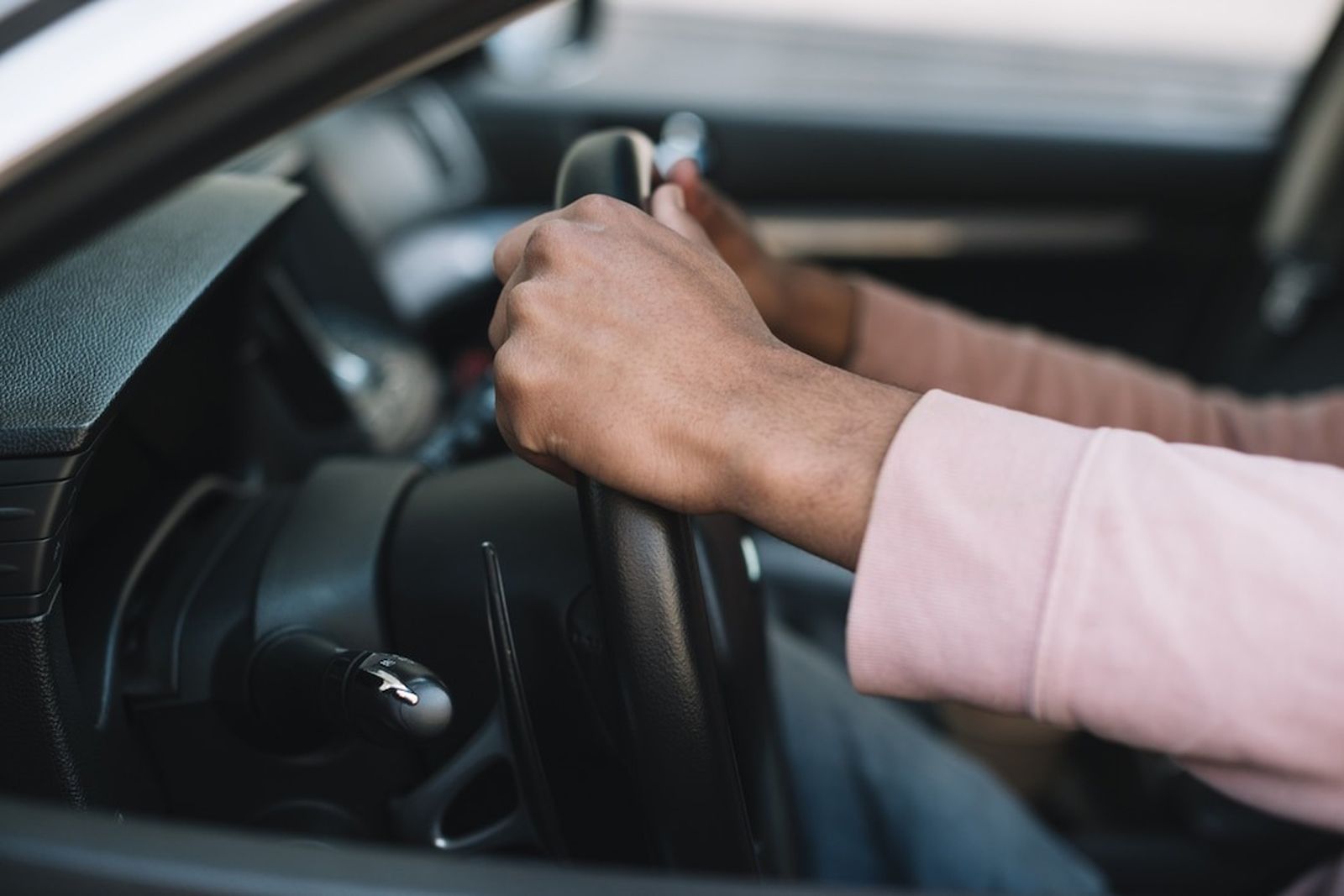 Person driving a car with a focus on the hands holding the steering wheel.