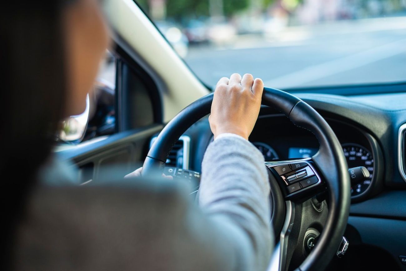 A person driving a car, with a focus on their hand on the steering wheel.