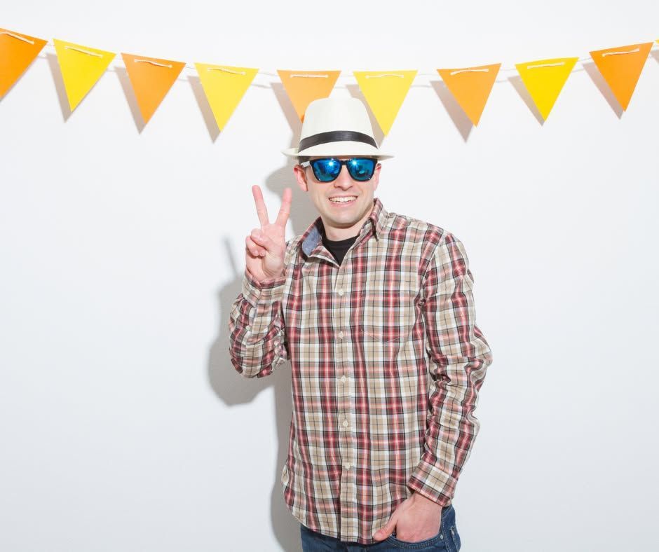 Person in sunglasses and a hat posing with a peace sign in front of yellow pennant flags.