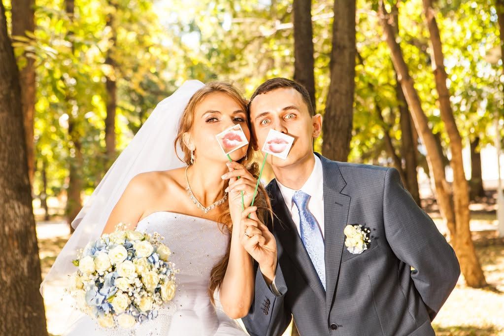 Bride and groom posing outdoors in a sunlit park, smiling and holding lollipops