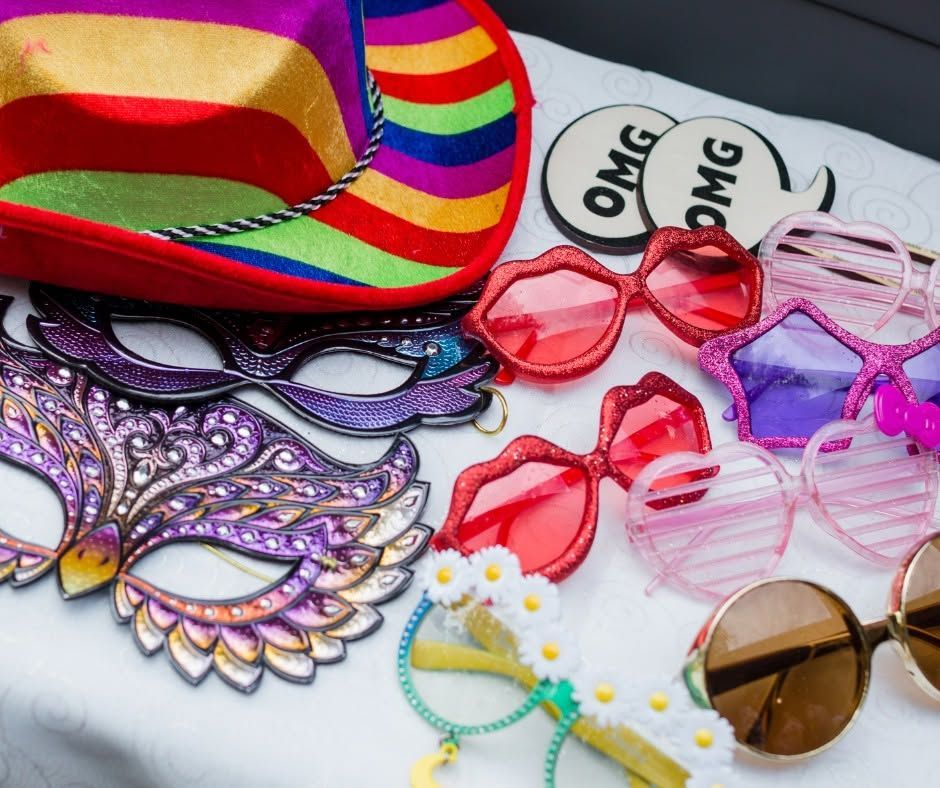 Colorful party glasses and masks, including rainbow, heart, and “OMG” styles, on a white surface.