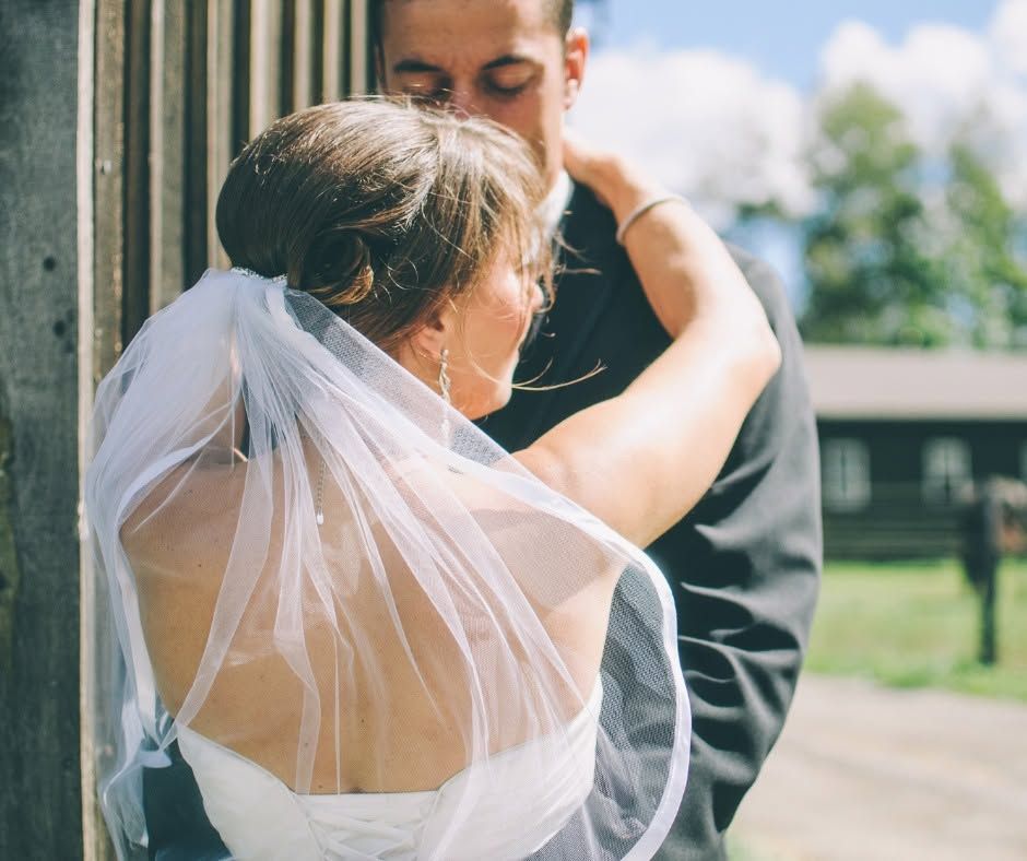 Bride in white veil embraces groom in a suit outdoors during a wedding ceremony