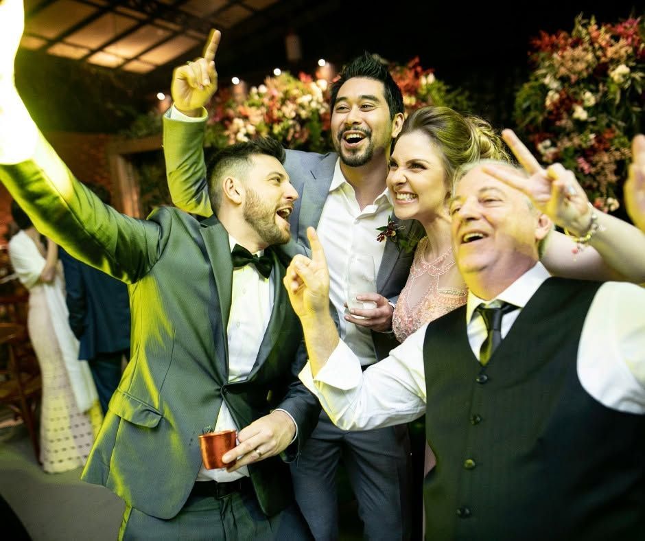 Four people in formal wear celebrating and laughing at a festive party, arms raised together.