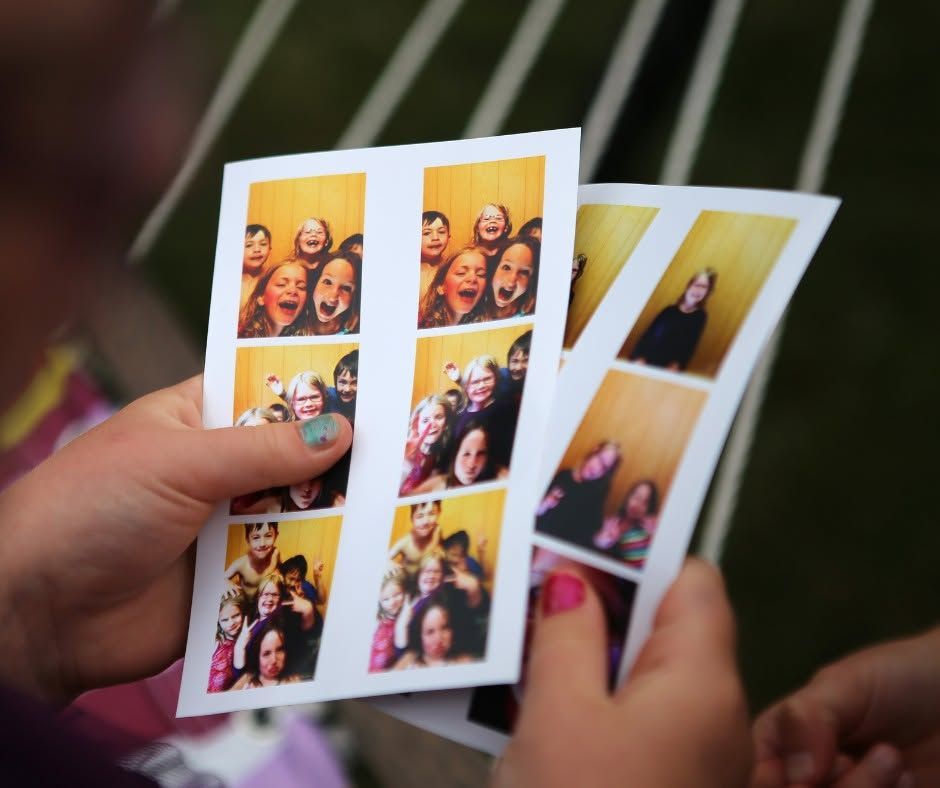 Hand holding three small photo prints with colorful snapshots, outdoors against a blurred background