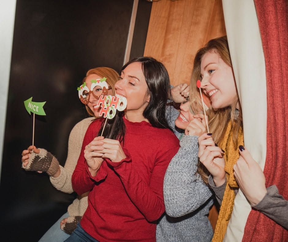 Three people smiling with party props and lollipops, posing by a curtain indoors