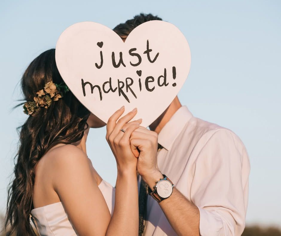 Couple kissing behind a heart-shaped sign reading “just married!”