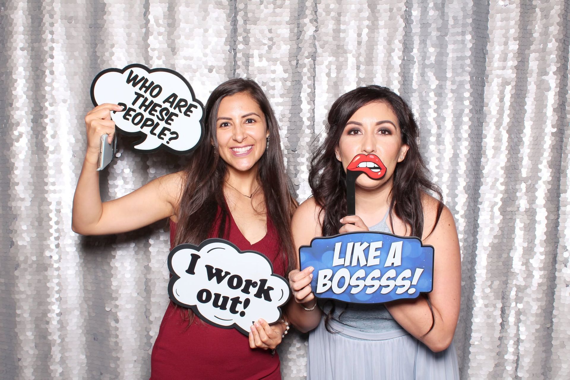 Three women posing at a party photo booth with speech props and a silver backdrop.